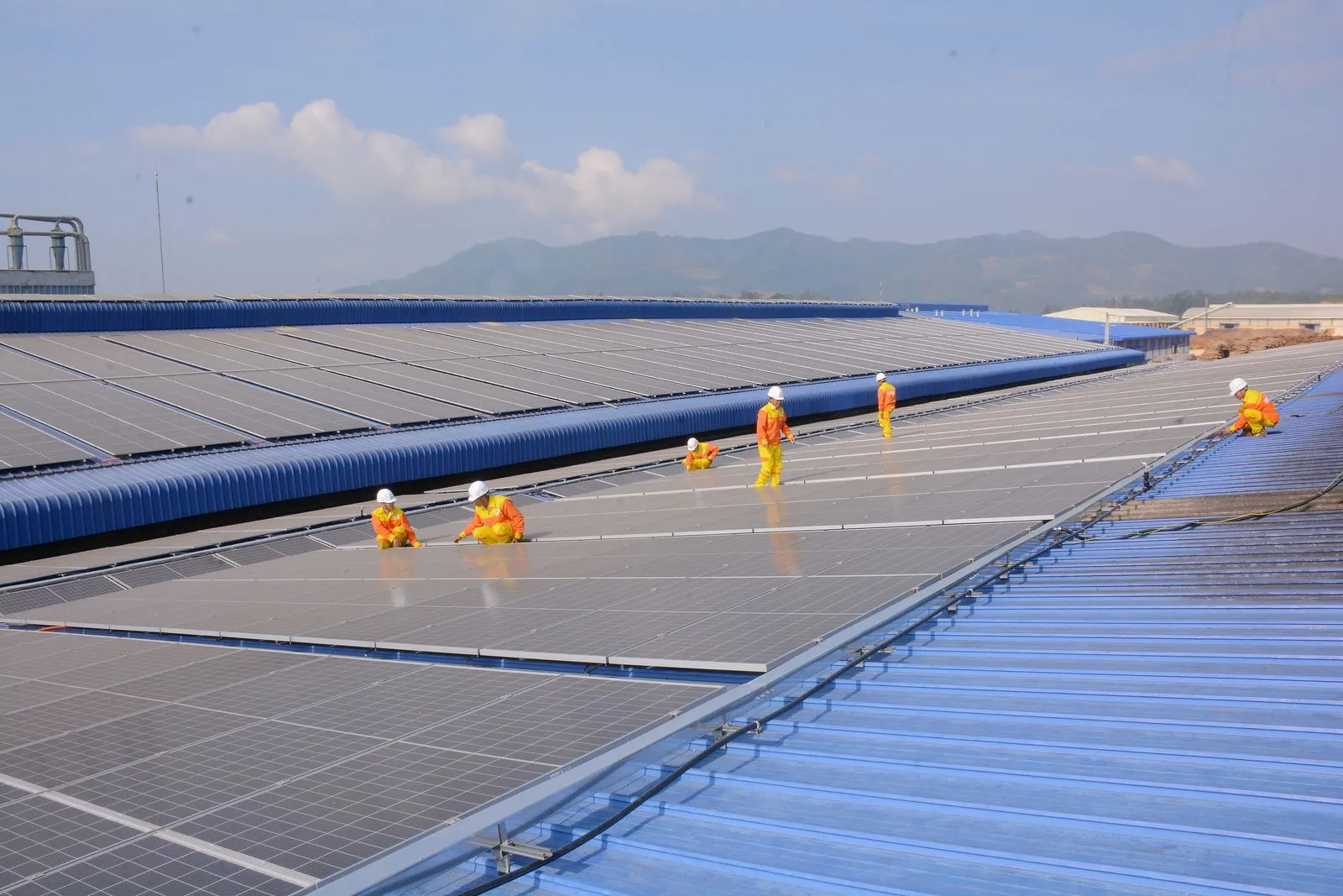 Workers installing solar panels on a large roof, highlighting renewable energy and sustainability.